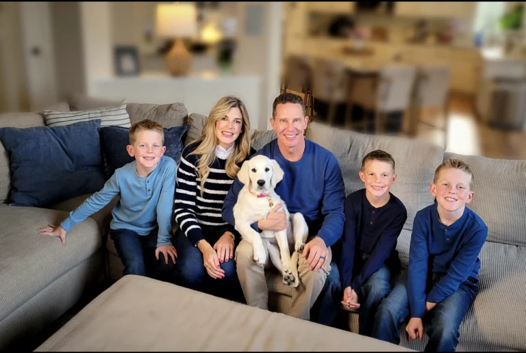 A family of five sitting together on a couch with their white dog.
